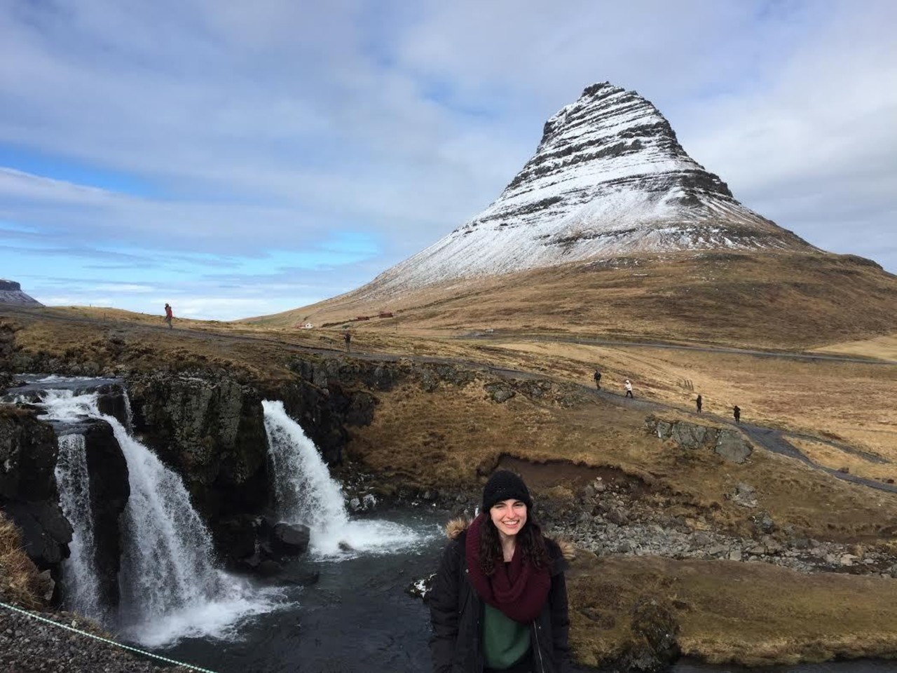 Sydney, Adventurer of the Week, is on Snæfellsnes peninsula posing for a photo in front of waterfall and Kirkjufell mountain