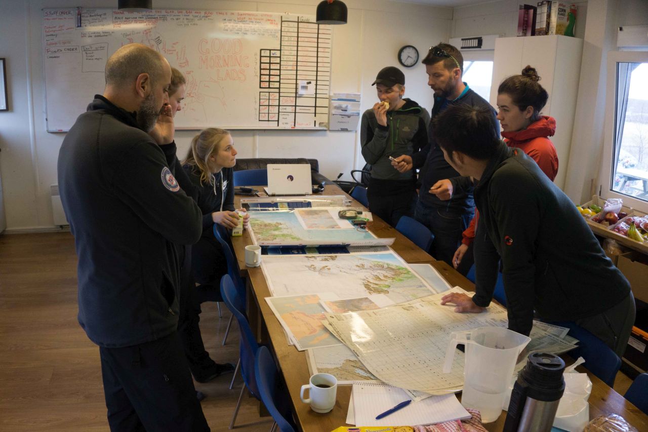 A group of people standing by tables looking at maps on a polar training course with Icelandic Mountain Guides