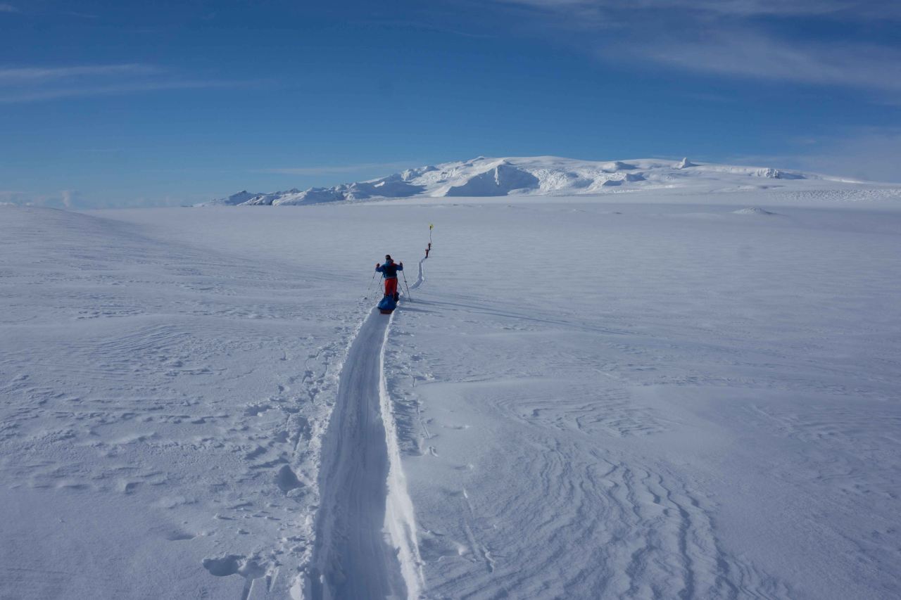 A group crossing a glacier on cross country skis with pulkas on a sunny day on a course with Icelandic Mountain Guides