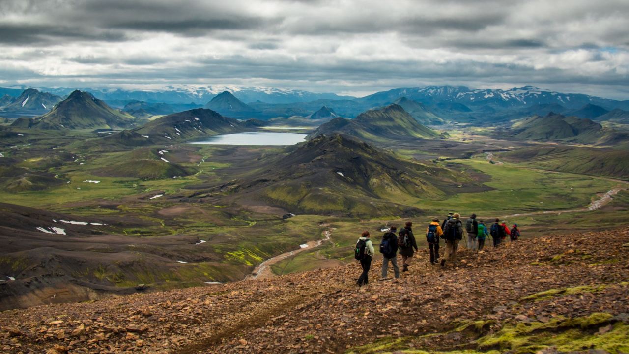 A group of people hiking toward green and black mountains in Iceland. Iceland hiking tours feature the best of the highlands.