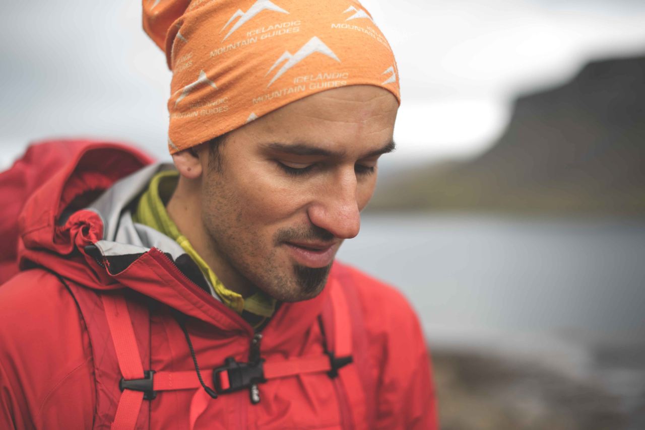 A man wearing a red jacket and an orange hat marked Icelandic Mountain Guides