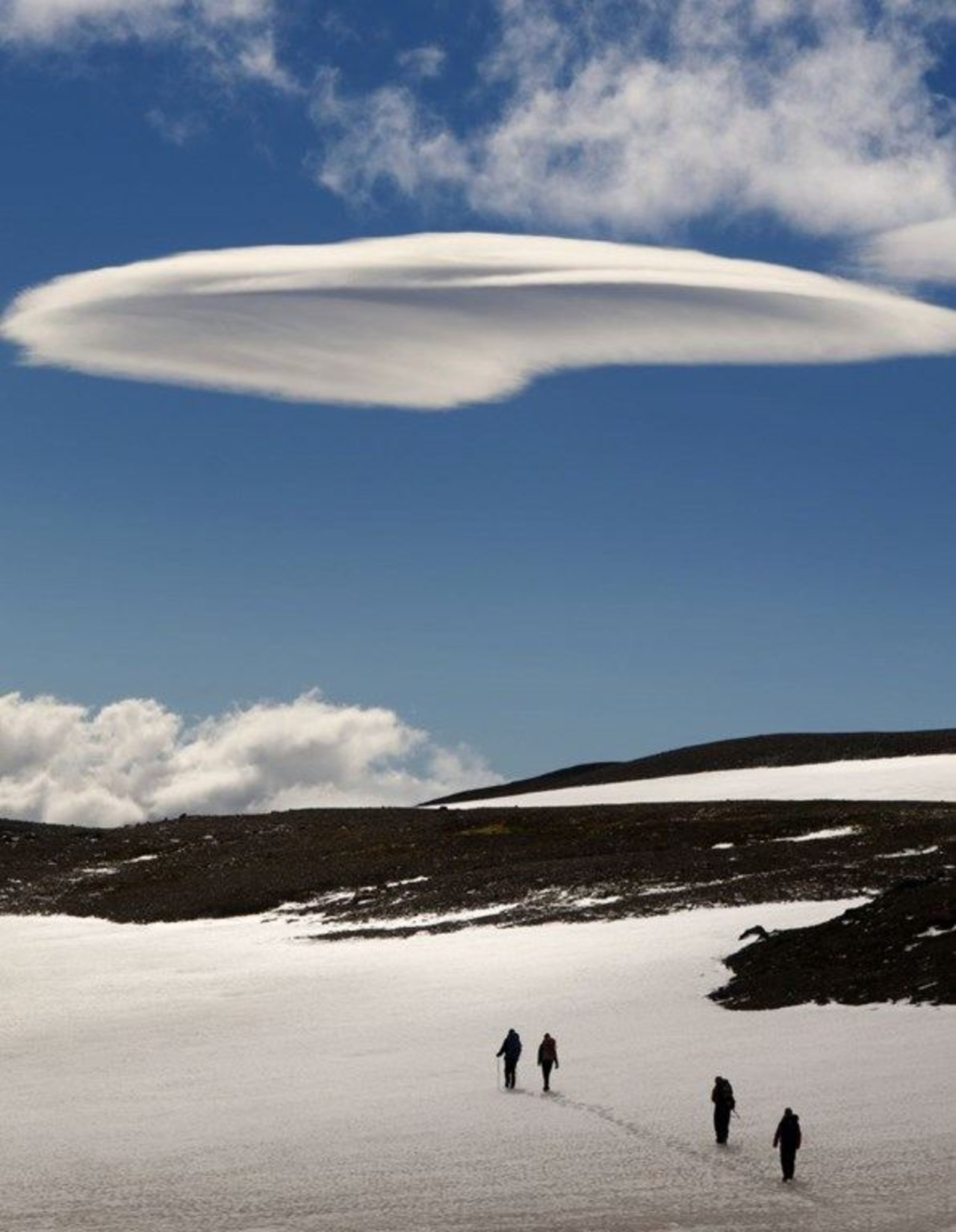 People hiking through snow on a summer day with a white cloud in the middle of the sky