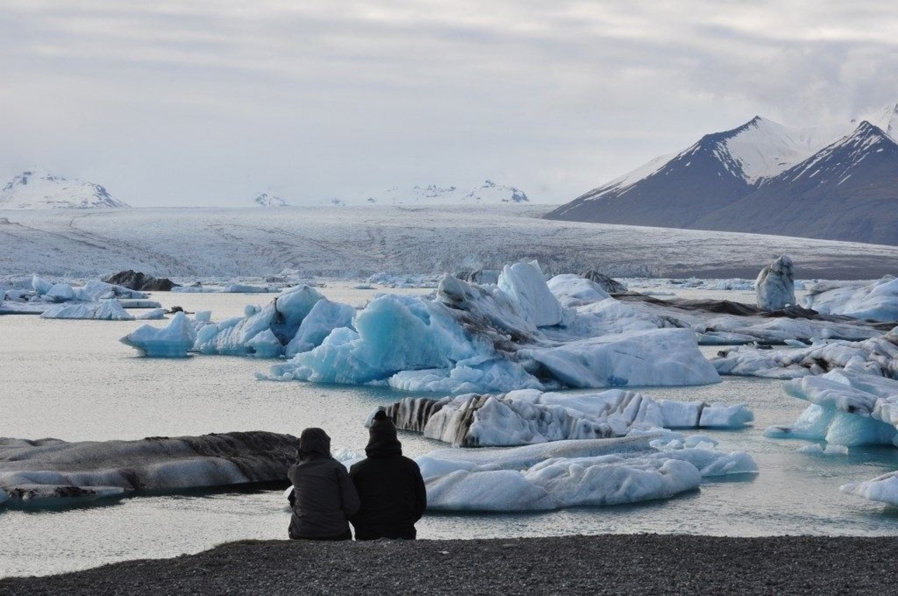 People admiring the ice bergs in Jökulsárlónwith snowy mountains in background